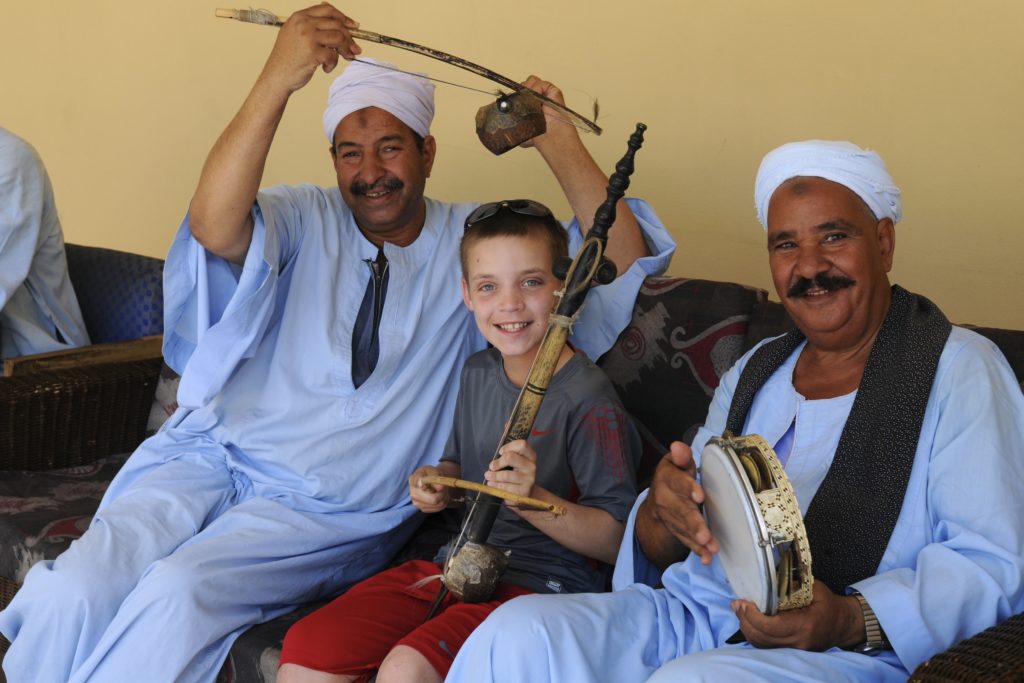 Young boy plays Egyptian instruments with two Egyptians.
